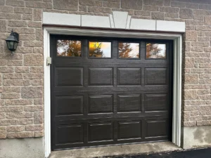 Black raised-panel garage door with four top windows in a brick opening