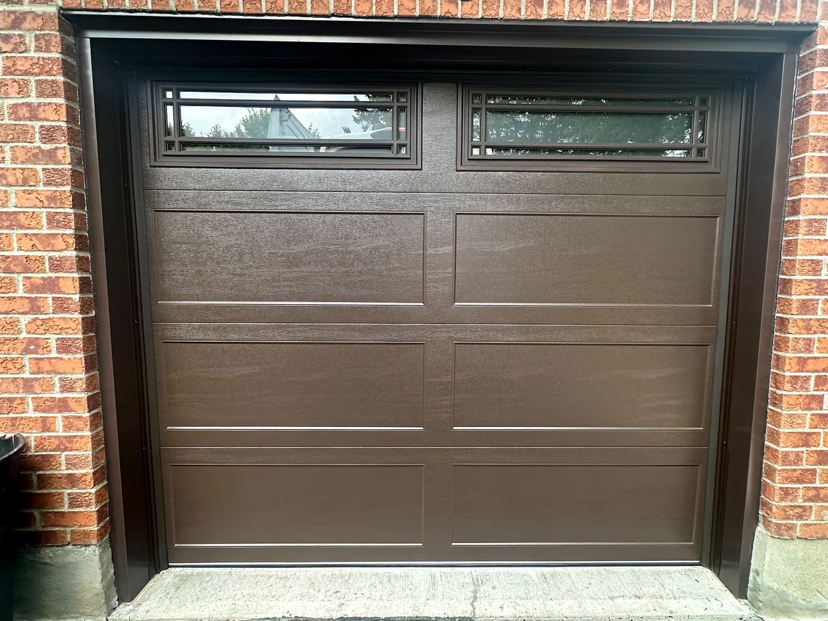 Brown carriage-style garage door with rectangular top windows and raised panels