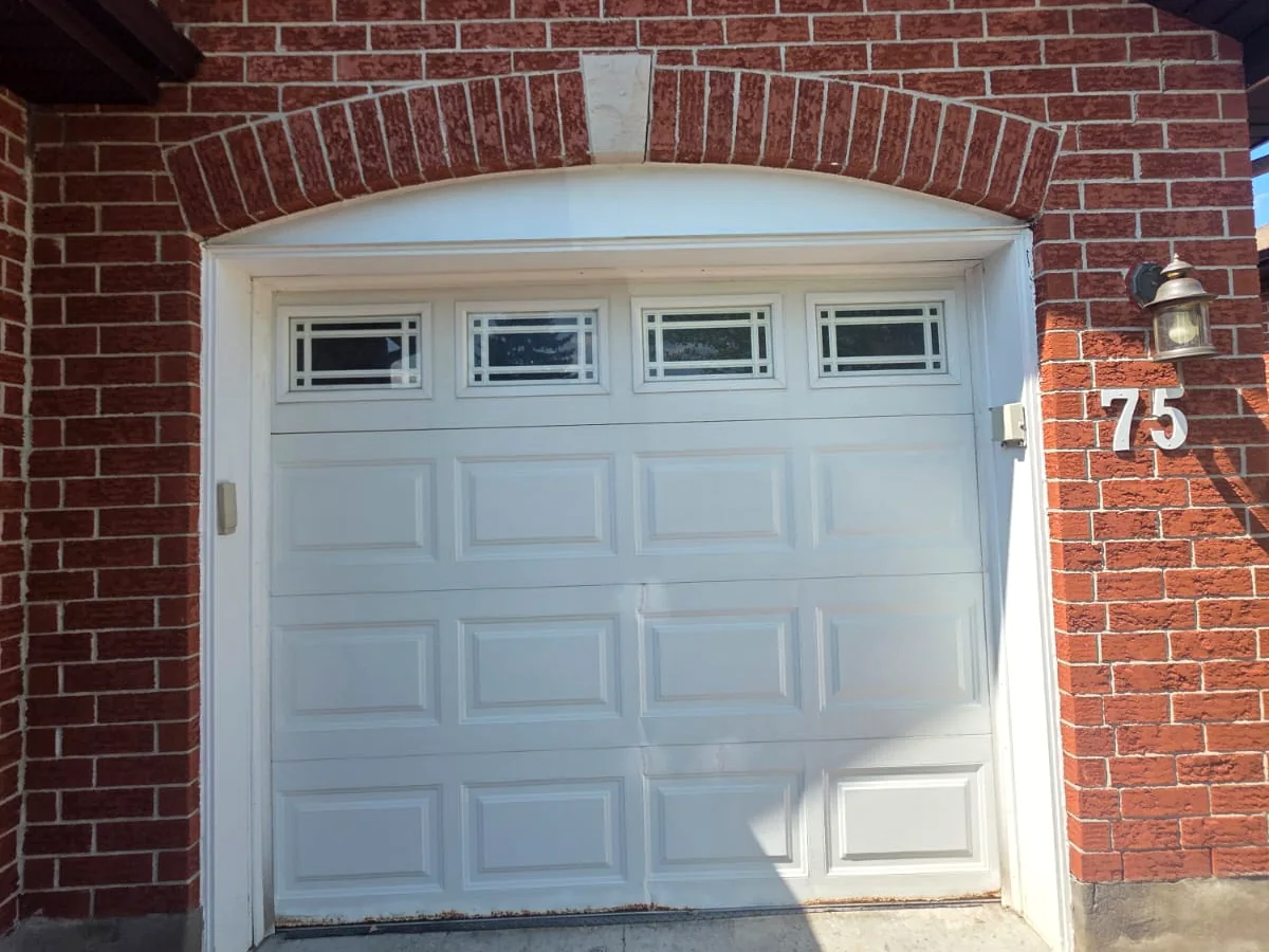 Older white sectional garage door with worn panels before replacement at a Calgary home