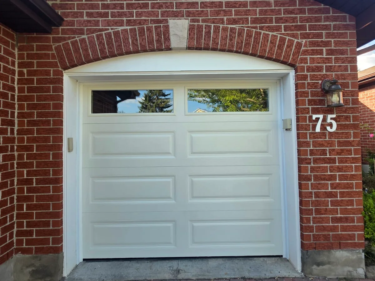 Completed white sectional garage door with top windows at a brick Calgary home