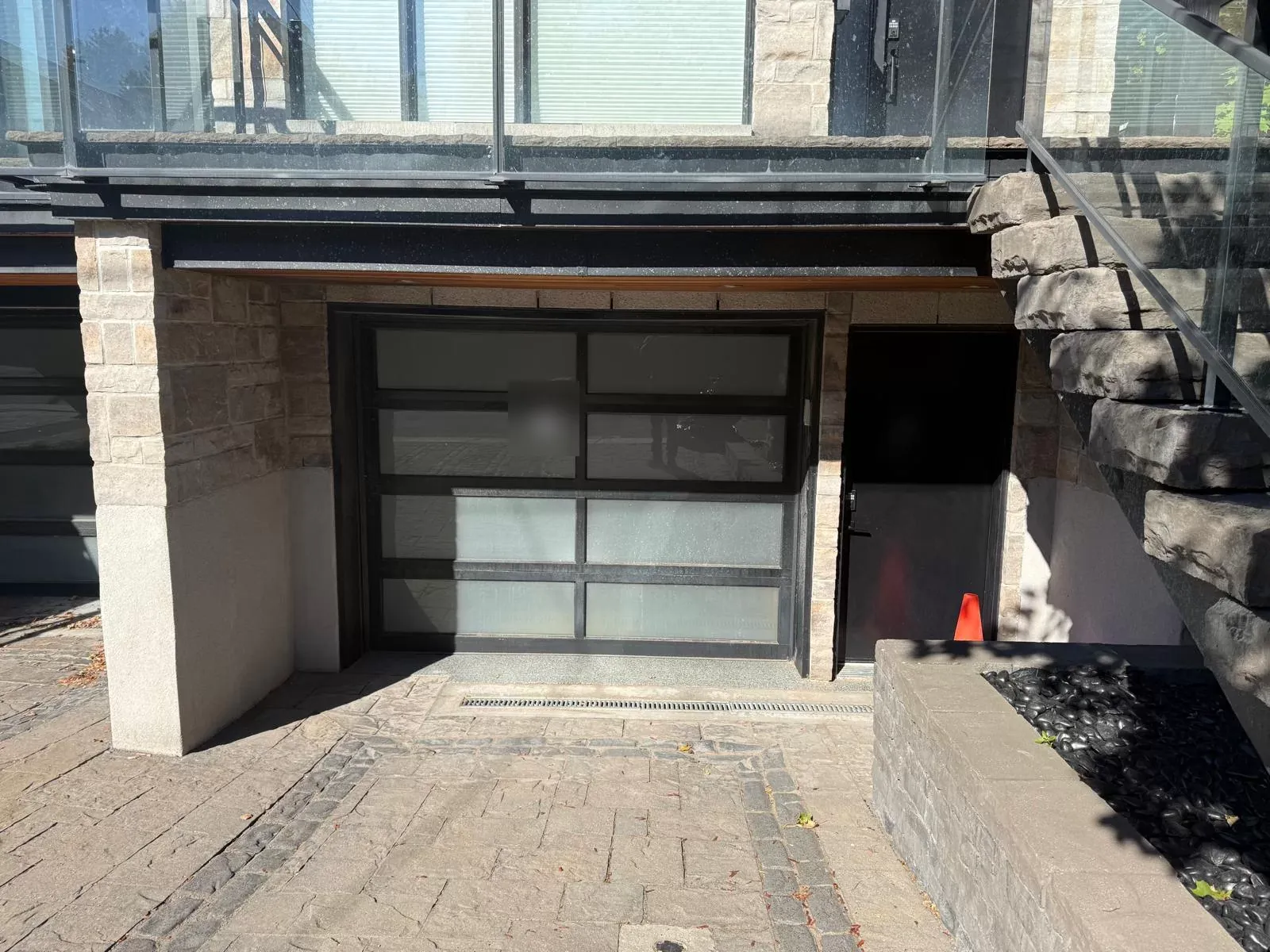 Full-view garage door with frosted glass panes in a black frame on a Calgary stone garage, before replacement