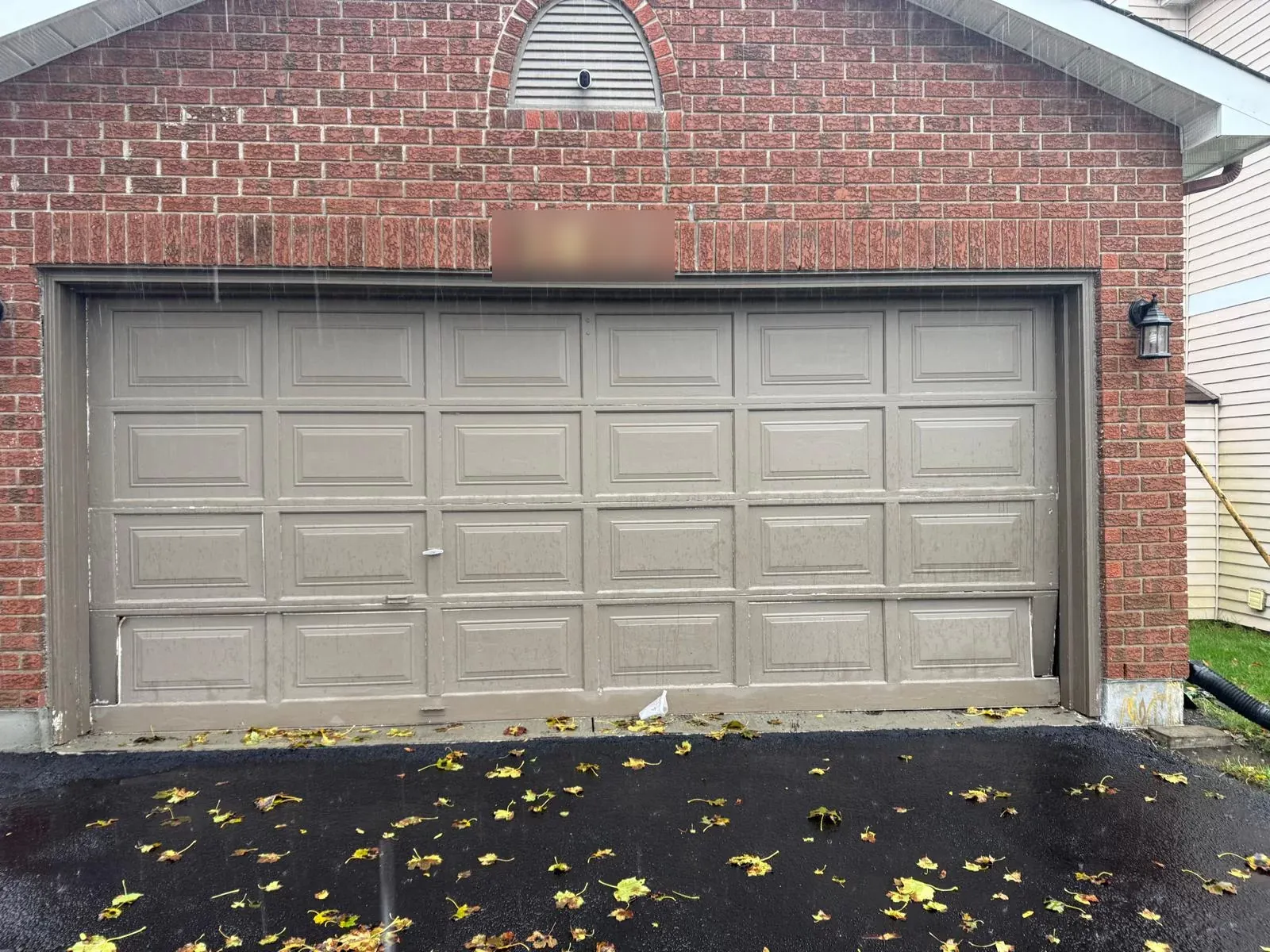 Old taupe raised-panel garage door on a Calgary brick garage before replacement